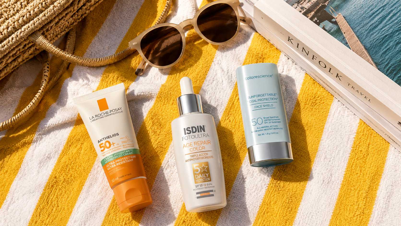 Flat lay of sunscreen products on a yellow striped beach towel with sunglasses, a woven beach bag, and a travel book under natural sunlight.